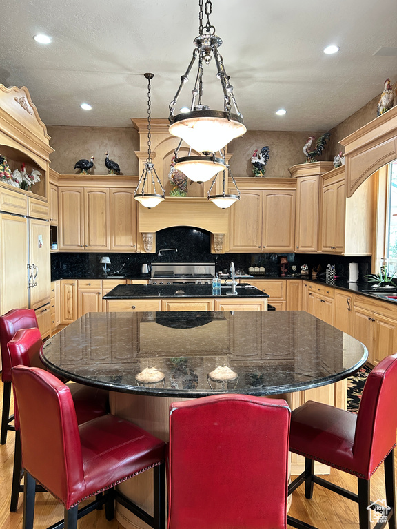 Kitchen with light wood-type flooring, a breakfast bar area, backsplash, a center island, and light brown cabinets