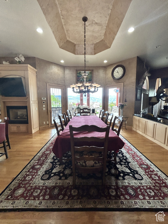 Dining area featuring a tray ceiling, an inviting chandelier, baseboards, and light wood finished floors