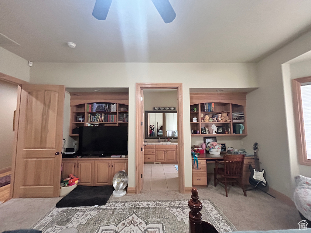 Bedroom featuring built in desk, light carpet, ensuite bathroom, and ceiling fan