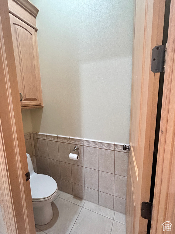 Bathroom featuring a wainscoted wall, toilet, tile walls, and tile patterned floors