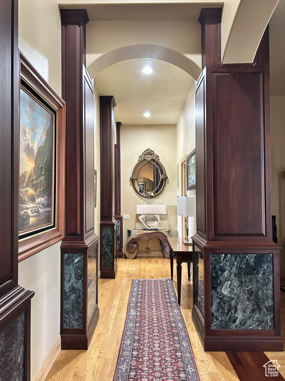Corridor featuring arched walkways, baseboards, light wood-style flooring, and recessed lighting