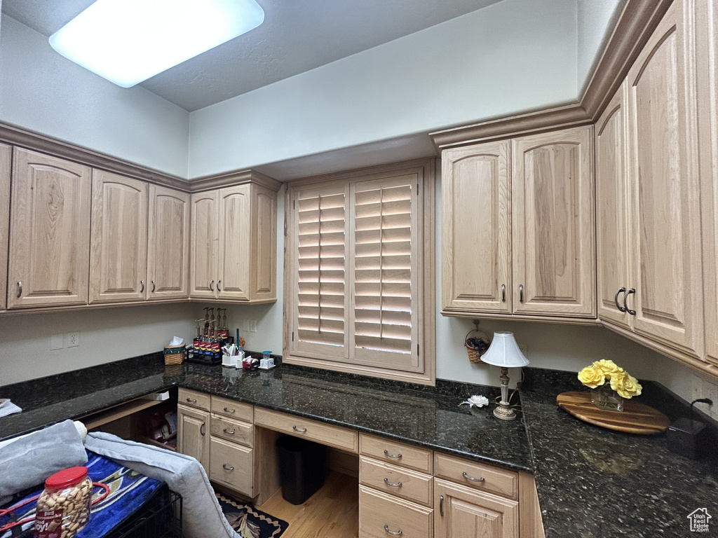 Kitchen featuring light brown cabinetry, dark stone countertops, and built in study area