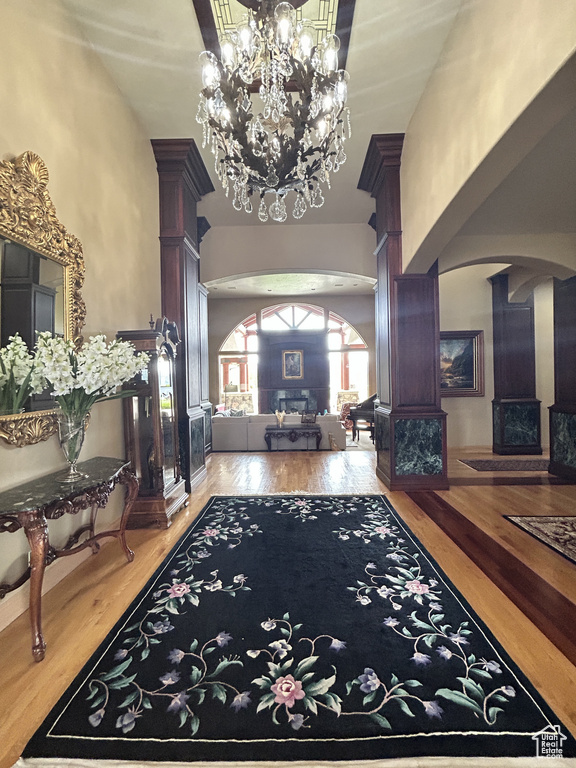 Entrance foyer featuring an inviting chandelier, wood finished floors, decorative columns, a towering ceiling, and arched walkways
