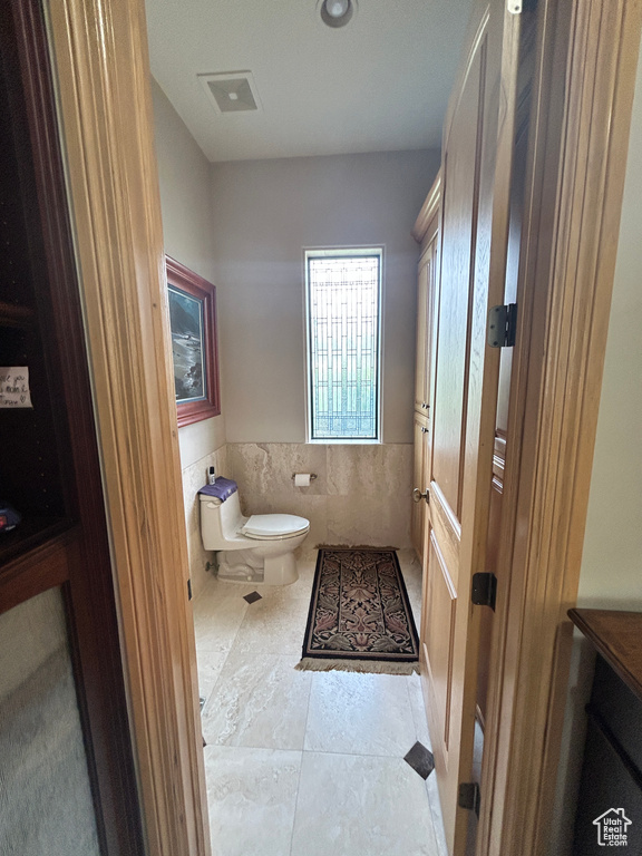 Half bath with tile walls, toilet, visible vents, tile patterned floors, and a wainscoted wall