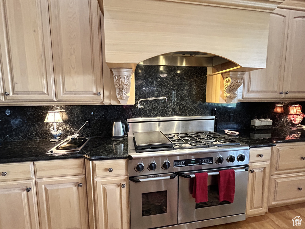 Kitchen featuring double oven range, custom exhaust hood, dark stone countertops, decorative backsplash, and arched walkways