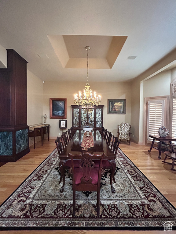 Dining space with a tray ceiling, an inviting chandelier, and light wood-style flooring
