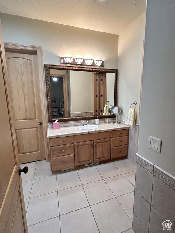 Bathroom featuring tile walls, tile patterned floors, vanity, and wainscoting
