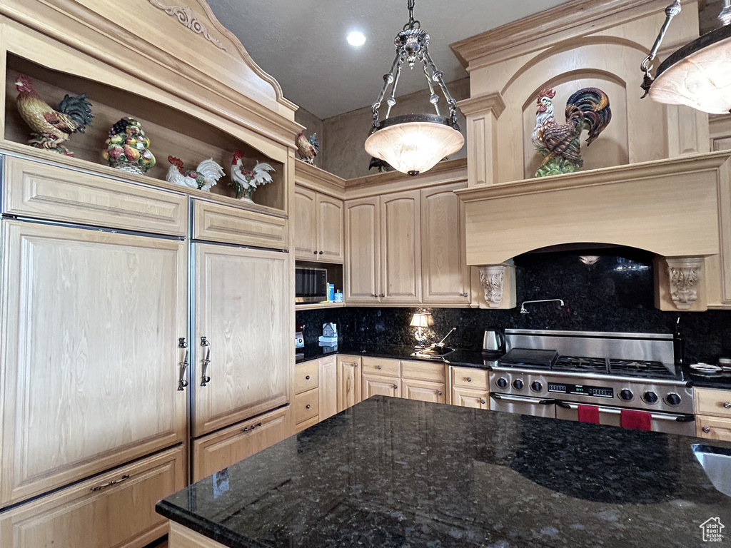 Kitchen featuring stainless steel gas range, tasteful backsplash, light brown cabinetry, and dark stone countertops