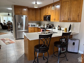 Kitchen featuring a sink, a peninsula, brown cabinets, light countertops, and appliances with stainless steel finishes