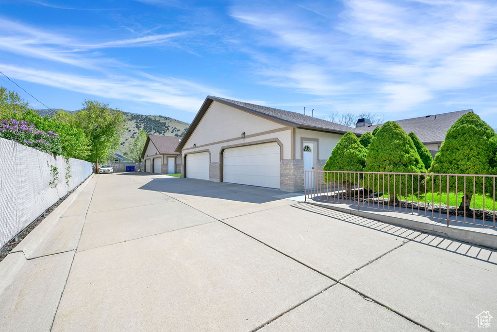 View of side of home featuring stucco siding, concrete driveway, fence, and an attached garage