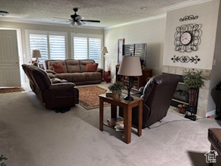 Living room with a ceiling fan, a textured ceiling, ornamental molding, and carpet floors
