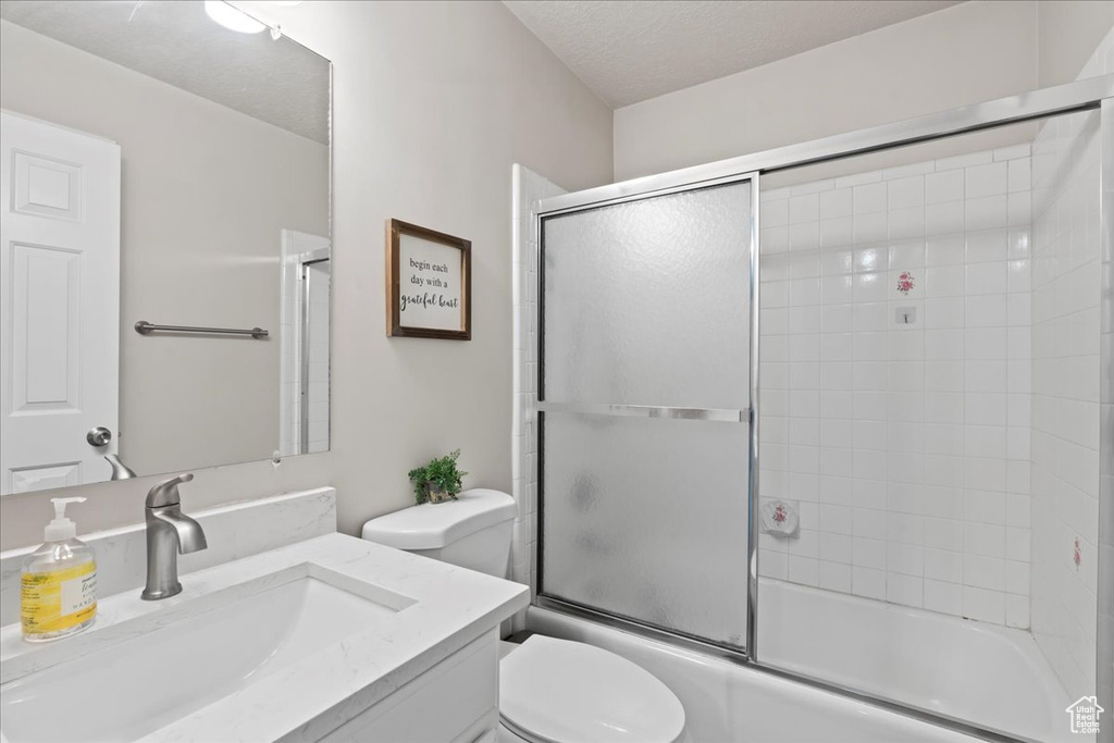 Bathroom with vanity, toilet, a textured ceiling, and enclosed tub / shower combo