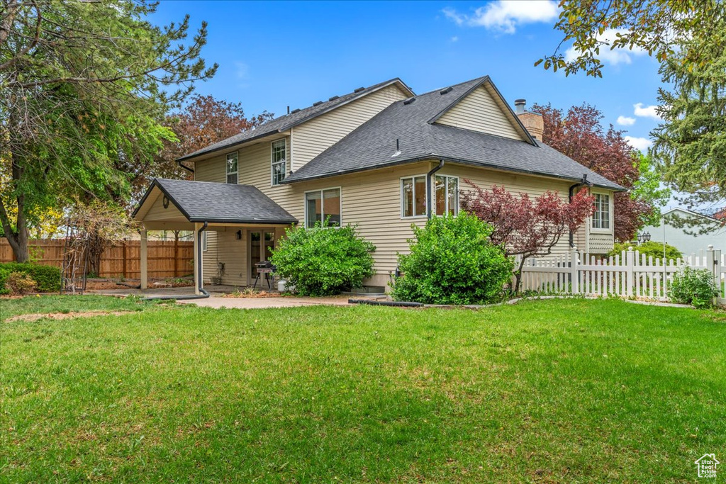 Back of property featuring a chimney, a yard, roof with shingles, and fence