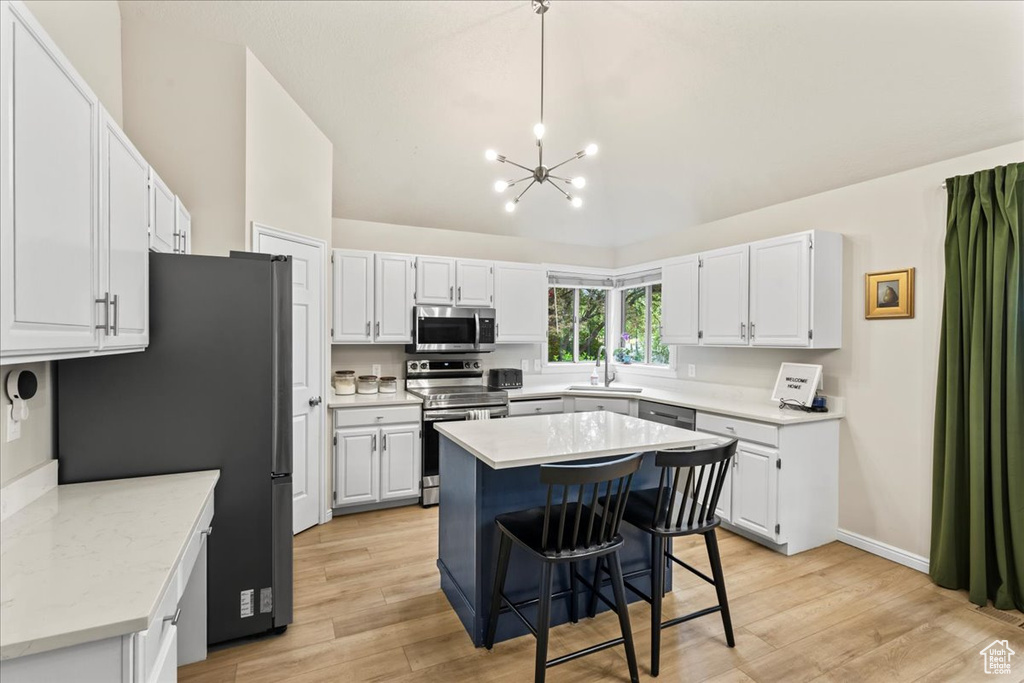 Kitchen featuring lofted ceiling, a notable chandelier, light wood-style flooring, a sink, and appliances with stainless steel finishes
