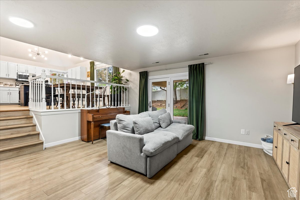Living area with stairs, visible vents, a chandelier, light wood-style flooring, and baseboards