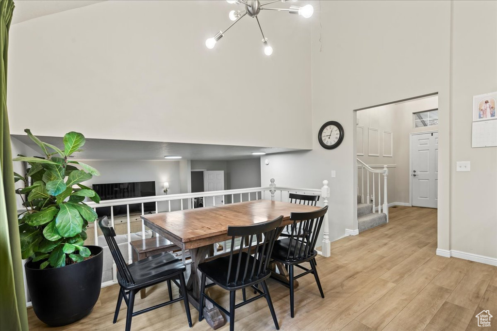 Dining space featuring an inviting chandelier, baseboards, light wood-style flooring, and a towering ceiling
