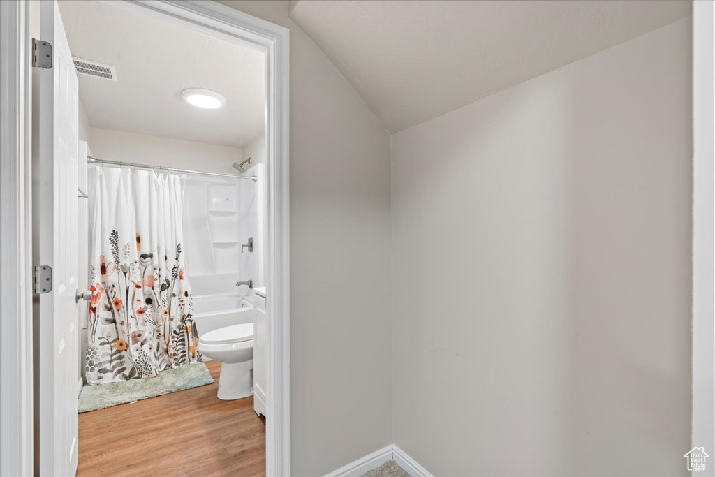 Full bath featuring toilet, shower / bath combo with shower curtain, wood finished floors, visible vents, and baseboards