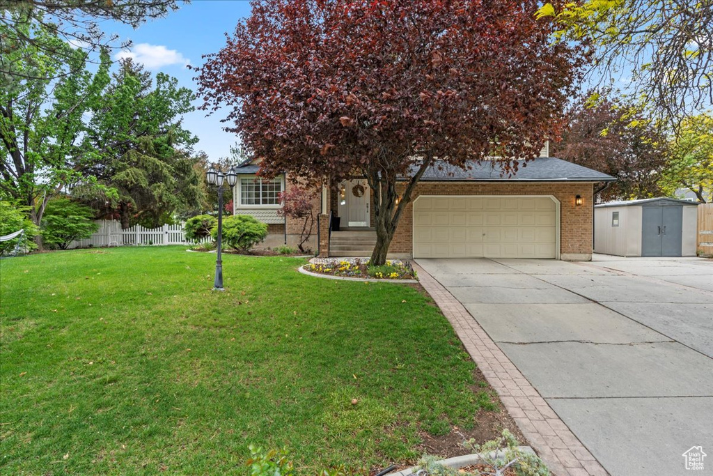 View of property hidden behind natural elements featuring a storage shed, fence, driveway, a garage, and a front yard