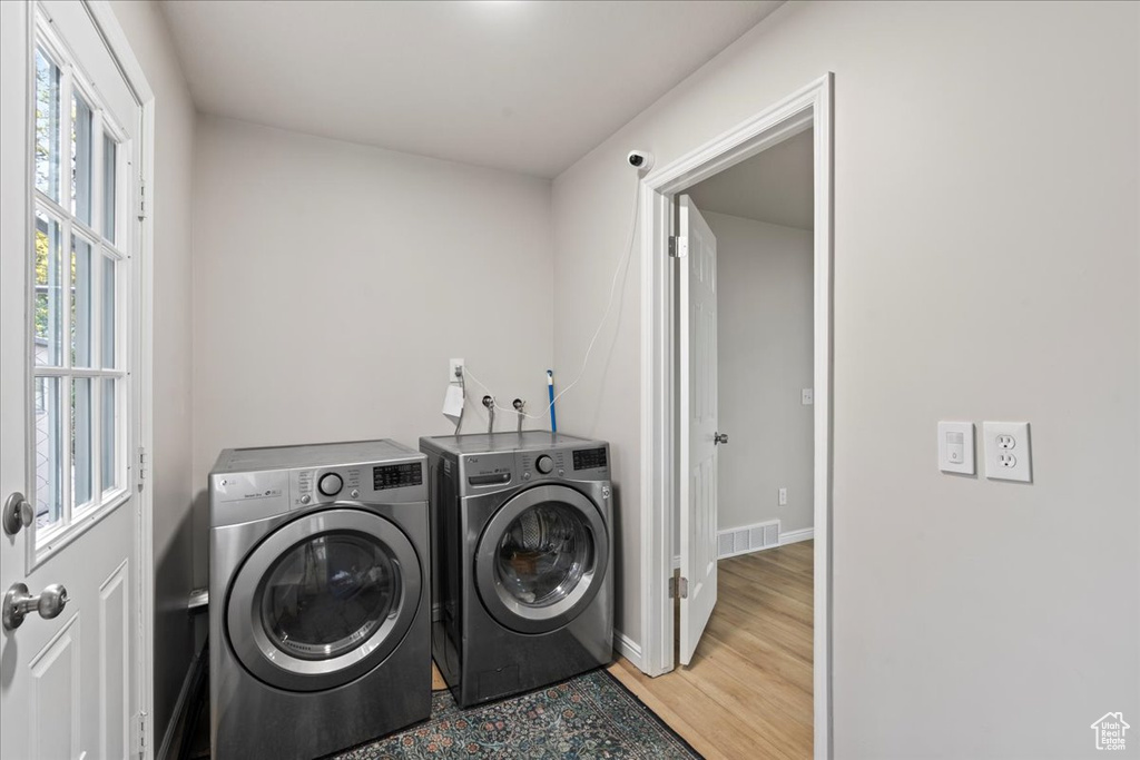 Clothes washing area featuring washing machine and clothes dryer, visible vents, wood finished floors, and baseboards