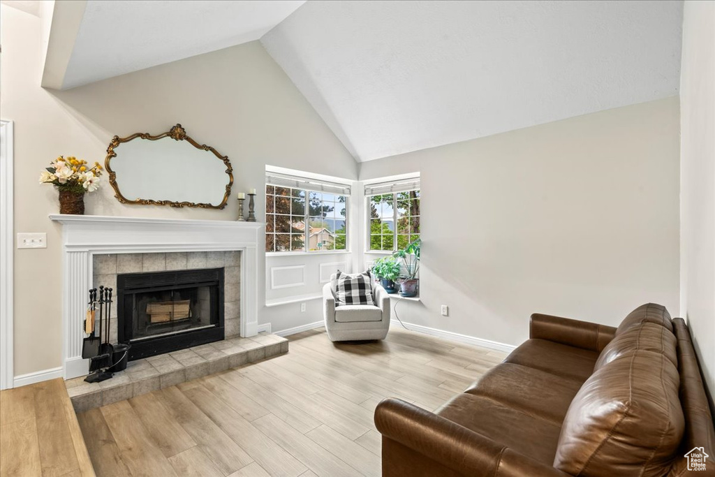 Living room featuring a tiled fireplace, wood finished floors, and high vaulted ceiling