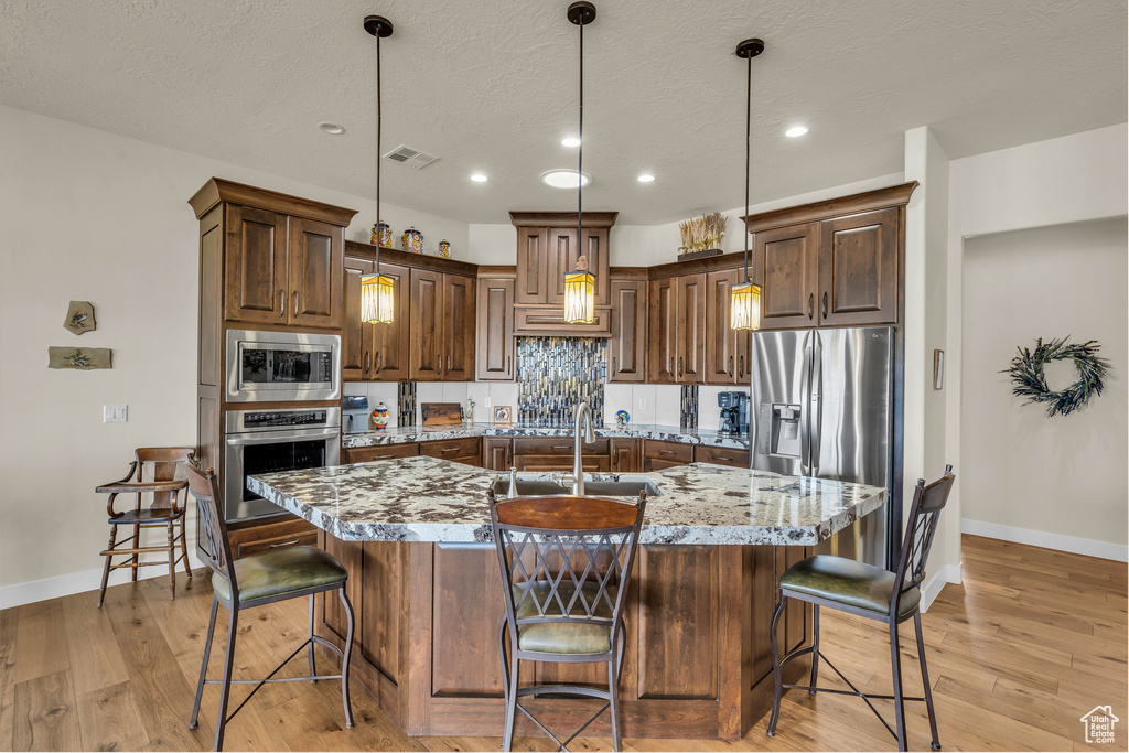 Kitchen with baseboards, a sink, an island with sink, and stainless steel appliances
