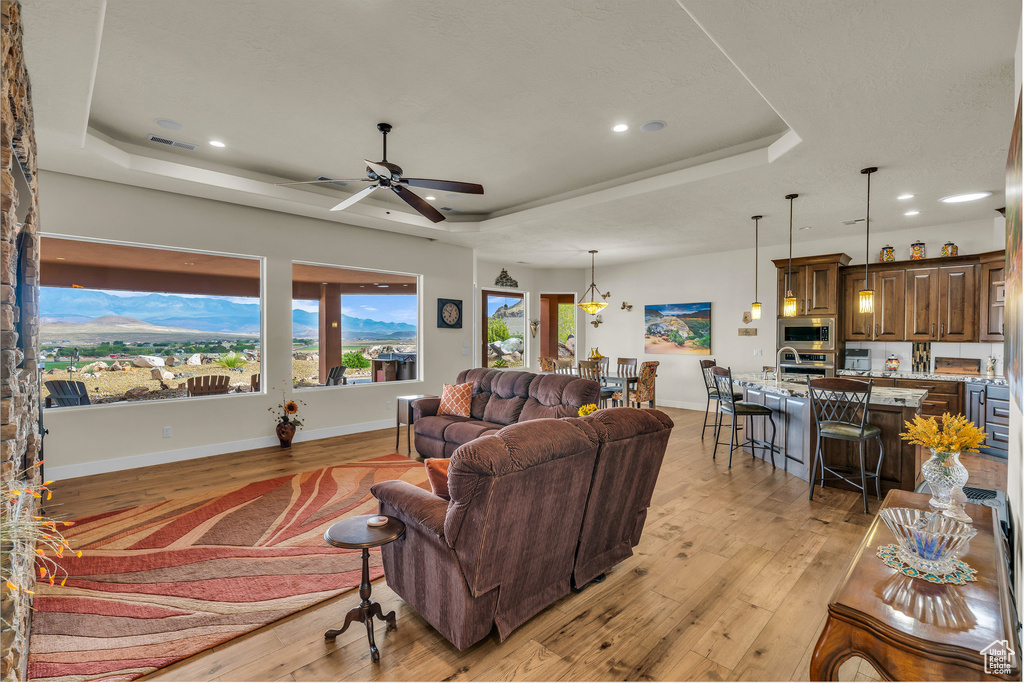 Living area featuring baseboards, recessed lighting, a raised ceiling, a ceiling fan, and light wood-style flooring