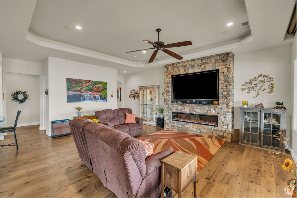 Living room featuring a ceiling fan, a tray ceiling, a stone fireplace, and wood finished floors