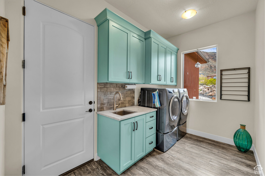 Laundry area featuring cabinet space, a sink, baseboards, light wood finished floors, and washer and clothes dryer