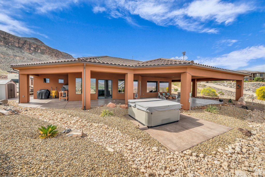 Back of property featuring a storage unit, a patio area, a hot tub, a mountain view, and a tile roof