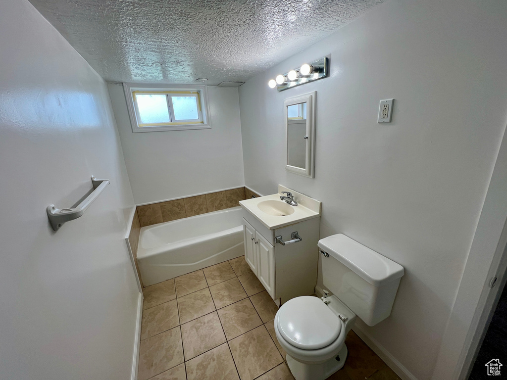 Full bath featuring a textured ceiling, toilet, tile patterned flooring, a garden tub, and vanity