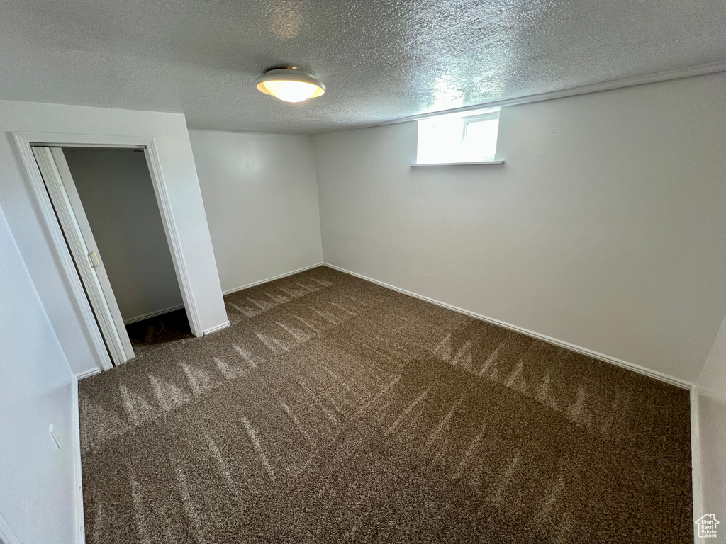 Below grade area with baseboards, dark carpet, and a textured ceiling