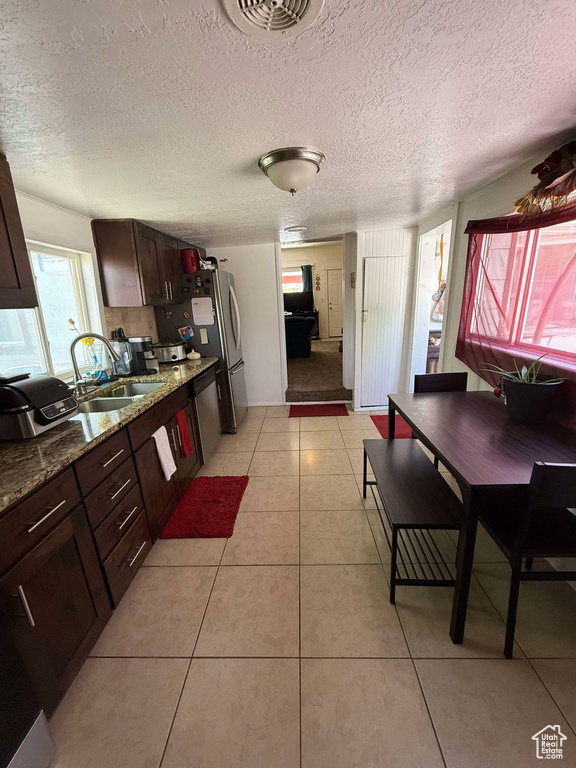 Kitchen with a sink, light tile patterned floors, dark brown cabinetry, stainless steel dishwasher, and a textured ceiling