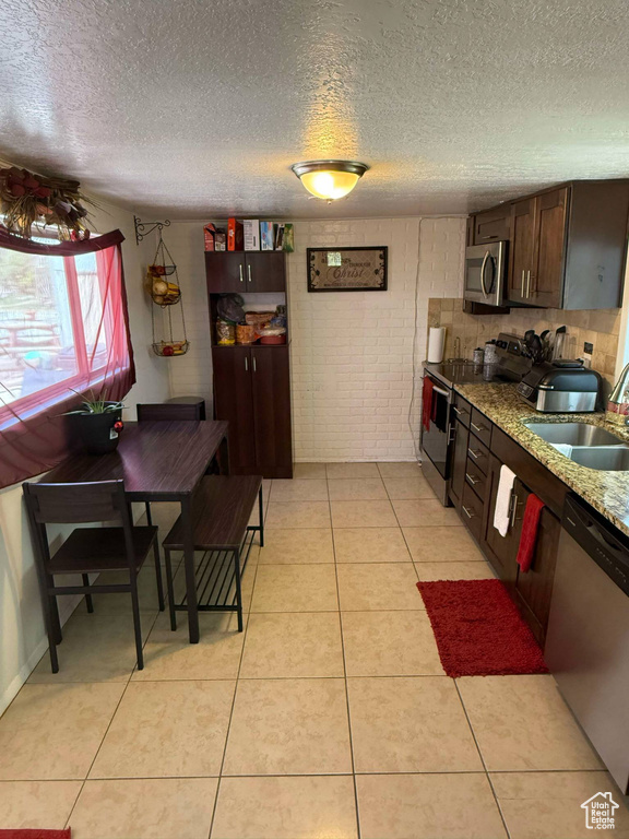 Kitchen featuring a sink, light tile patterned flooring, dark brown cabinetry, a textured ceiling, and appliances with stainless steel finishes