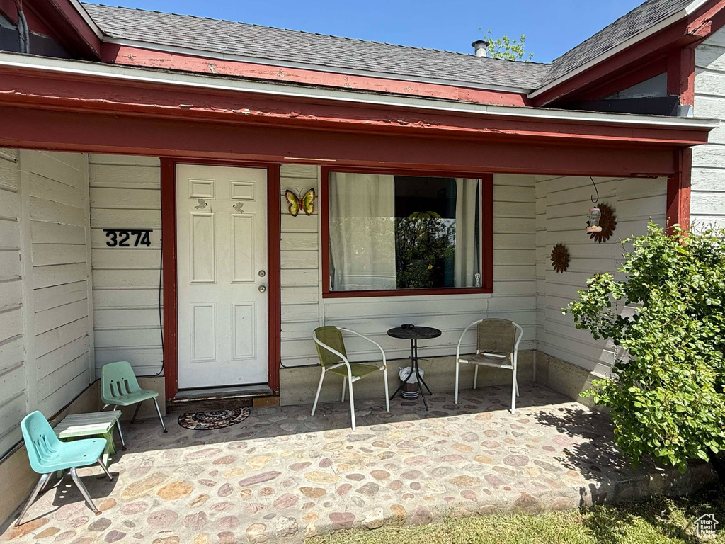 View of exterior entry featuring a shingled roof and a patio area
