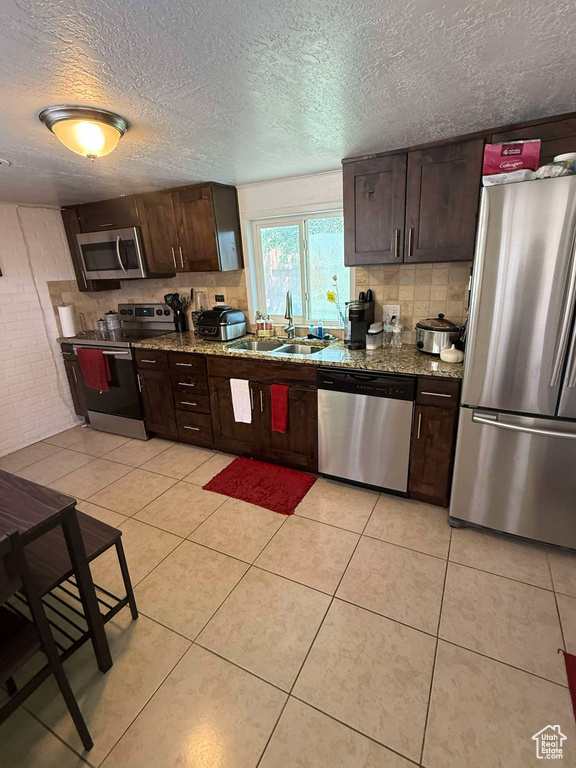 Kitchen with appliances with stainless steel finishes, dark brown cabinets, backsplash, a sink, and a textured ceiling