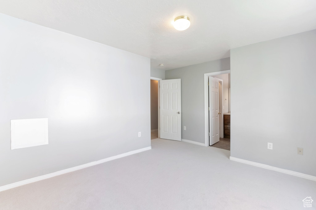 Unfurnished bedroom with ensuite bath, light carpet, and baseboards