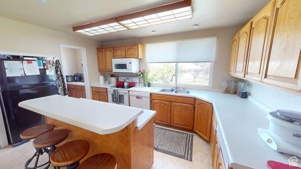 Kitchen featuring white appliances, a sink, a kitchen breakfast bar, and light countertops