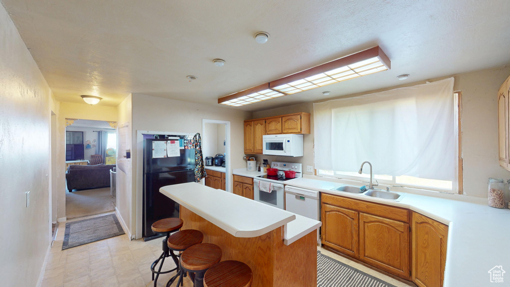 Kitchen featuring a breakfast bar area, a center island, a sink, white appliances, and light countertops