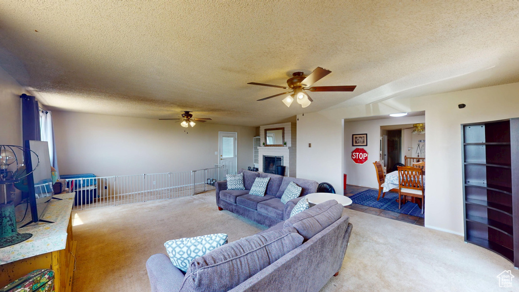 Living room with light colored carpet, a ceiling fan, a textured ceiling, and a fireplace