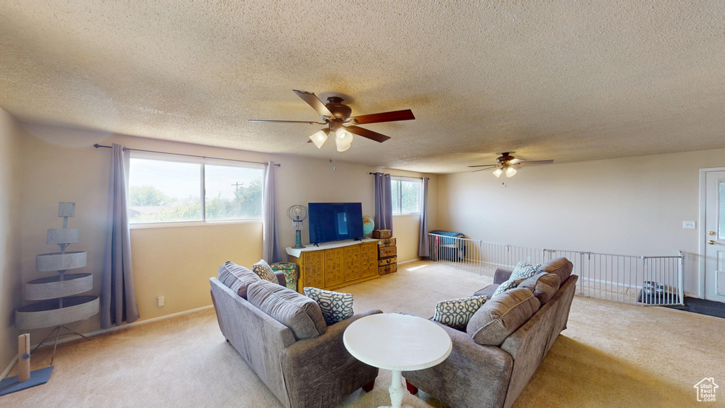 Living room featuring ceiling fan, light carpet, and a textured ceiling