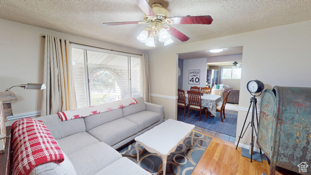Living area with a ceiling fan, a textured ceiling, and wood finished floors