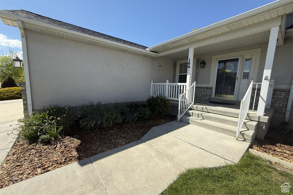 View of exterior entry with covered porch, roof with shingles, and stucco siding