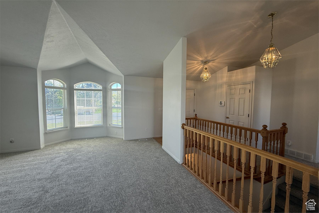 Carpeted empty room featuring baseboards, lofted ceiling, and a notable chandelier