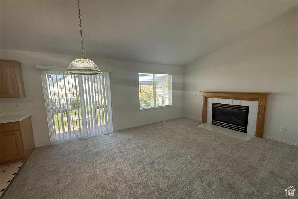 Unfurnished living room with vaulted ceiling, light carpet, baseboards, and a tile fireplace