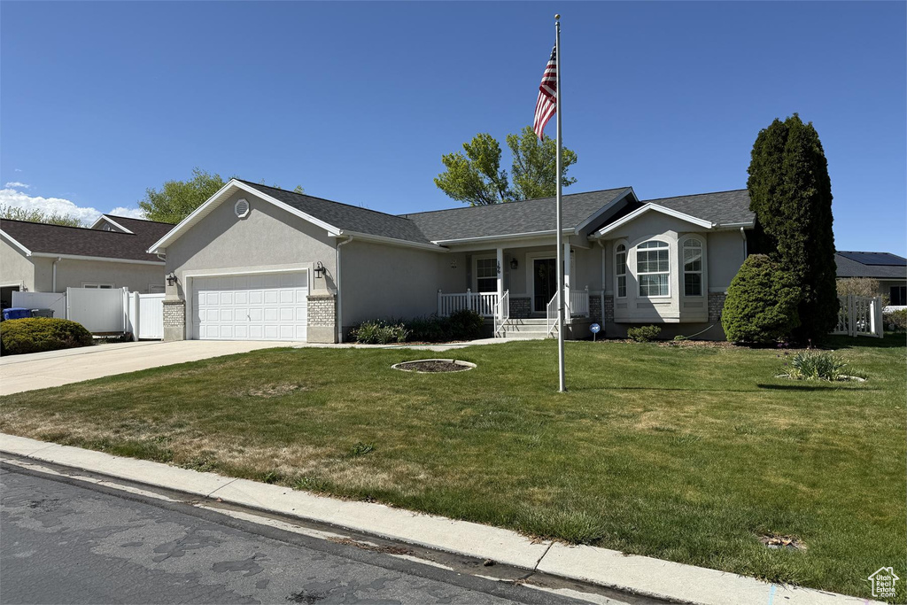 Ranch-style house featuring an attached garage, stucco siding, concrete driveway, a front yard, and a porch