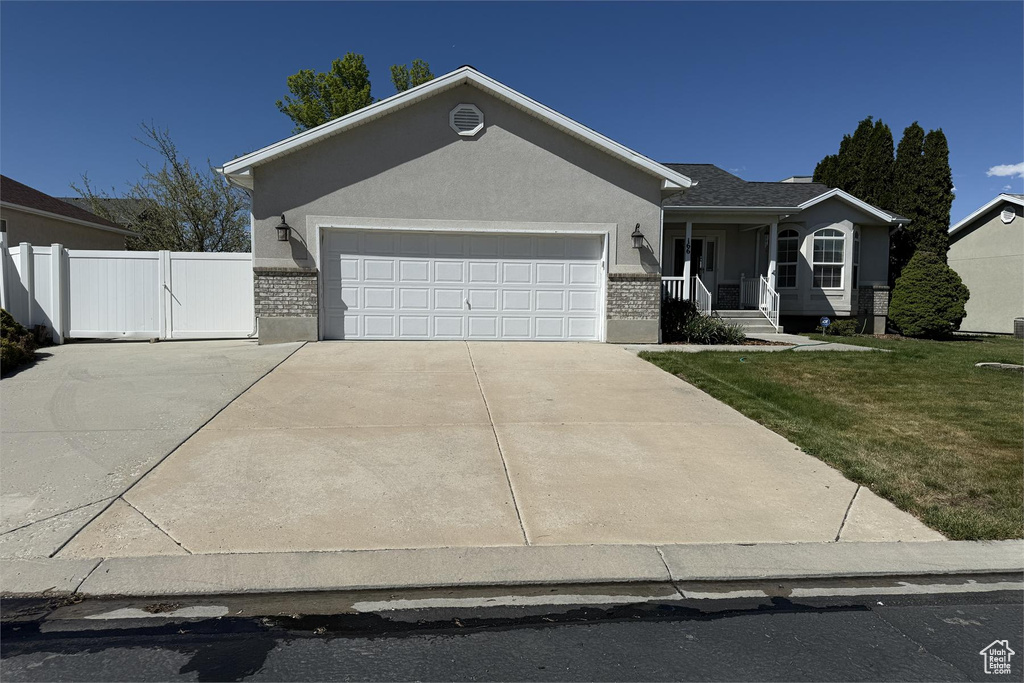 Ranch-style home with covered porch, an attached garage, fence, a front lawn, and driveway