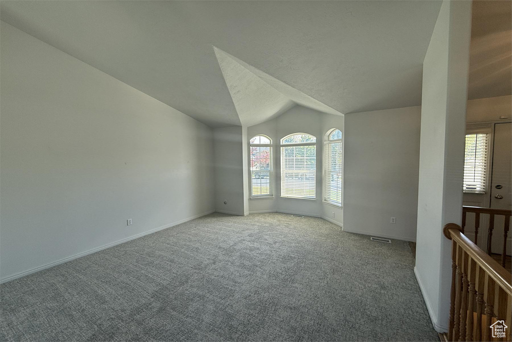 Carpeted spare room featuring baseboards, visible vents, and vaulted ceiling