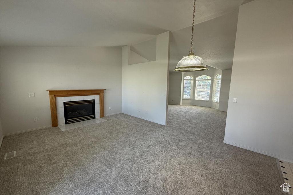 Unfurnished living room featuring a tile fireplace, visible vents, carpet, and high vaulted ceiling