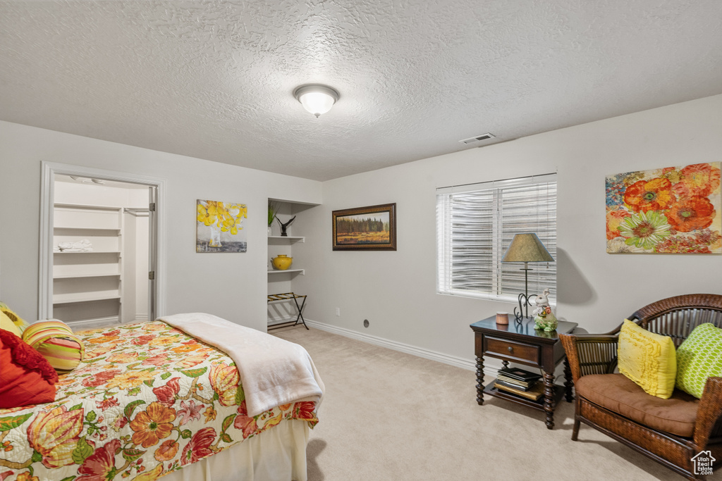 Bedroom with light colored carpet, visible vents, a textured ceiling, baseboards, and a spacious closet