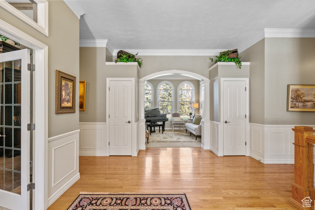 Entrance foyer with arched walkways, a wainscoted wall, light wood finished floors, ornamental molding, and a decorative wall